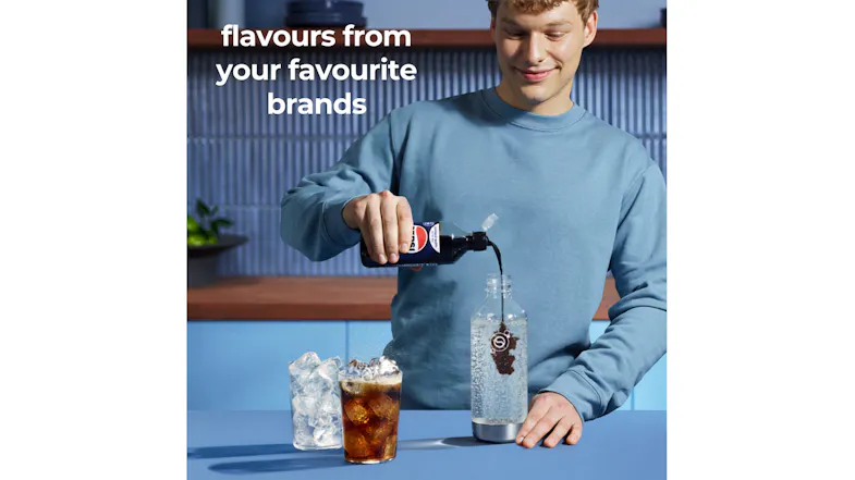 Sparkling water bottle with cola-flavoured syrup being poured beside iced drink glasses on a blue countertop Sparkling water bottle with cola-flavoured syrup being poured beside iced drink glasses on a blue countertop