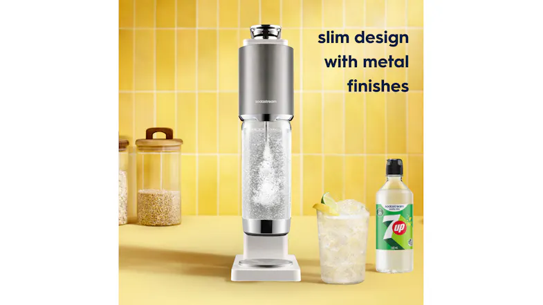 Warm white and silver SodaStream sparkling water maker on a kitchen counter with a 7UP syrup bottle and sparkling drink Warm white and silver SodaStream sparkling water maker on a kitchen counter with a 7UP syrup bottle and sparkling drink