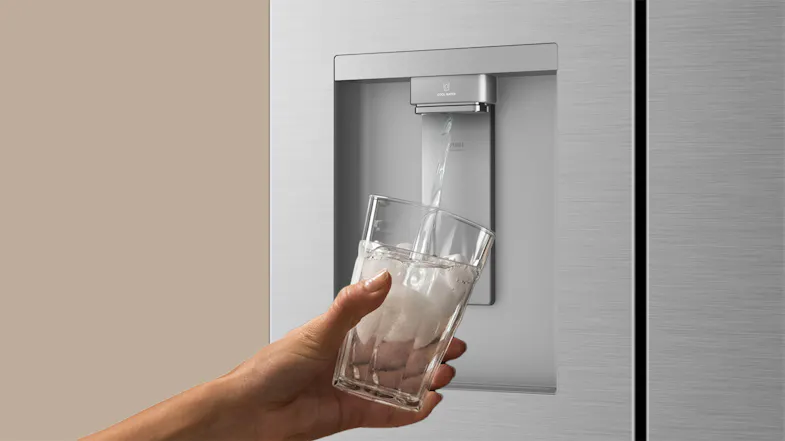 Silver refrigerator water dispenser dispensing chilled water into a clear glass with ice Silver refrigerator water dispenser dispensing chilled water into a clear glass with ice