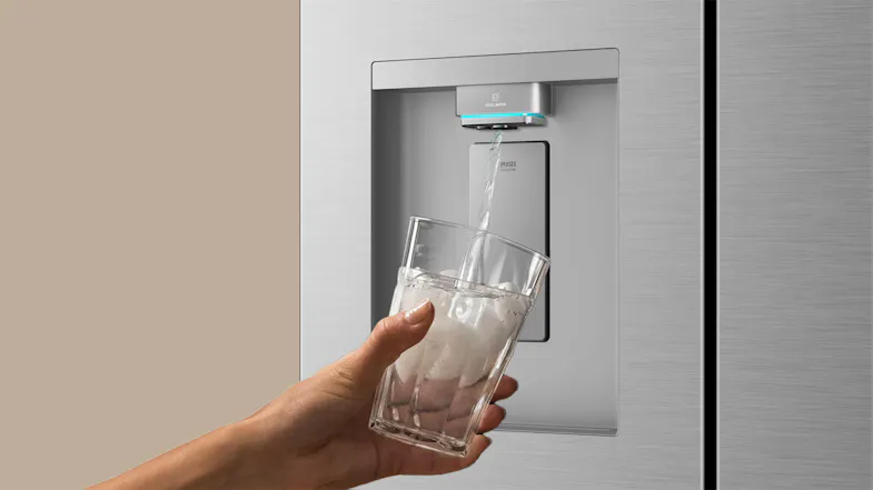 Close-up of a silver refrigerator water dispenser dispensing water into a clear glass with ice Close-up of a silver refrigerator water dispenser dispensing water into a clear glass with ice
