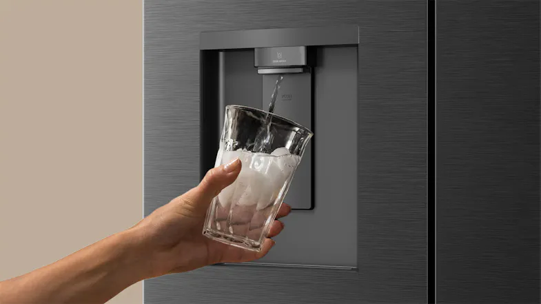 Close-up of a black refrigerator water dispenser dispensing chilled water into an ice-filled glass Close-up of a black refrigerator water dispenser dispensing chilled water into an ice-filled glass