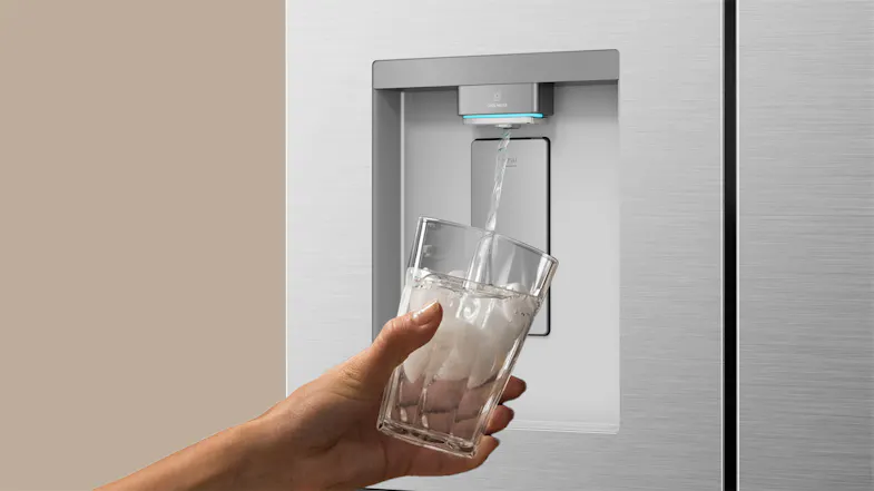 Silver refrigerator water dispenser dispensing chilled water into a clear drinking glass Silver refrigerator water dispenser dispensing chilled water into a clear drinking glass