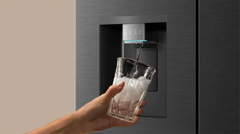 Close-up view of a black refrigerator water dispenser dispensing water and ice into a clear drinking glass Close-up view of a black refrigerator water dispenser dispensing water and ice into a clear drinking glass