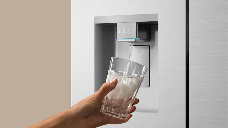 Close-up of a silver refrigerator water dispenser filling a clear drinking glass with ice water Close-up of a silver refrigerator water dispenser filling a clear drinking glass with ice water