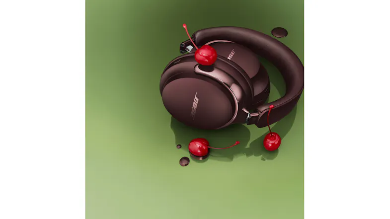 Folded QuietComfort Ultra headphones styled with fresh cherries on a green background Folded QuietComfort Ultra headphones styled with fresh cherries on a green background