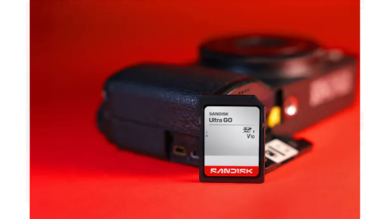 Front view of a SanDisk Ultra GO SDHC UHS-I memory card standing in front of a black camera on a red surface Front view of a SanDisk Ultra GO SDHC UHS-I memory card standing in front of a black camera on a red surface