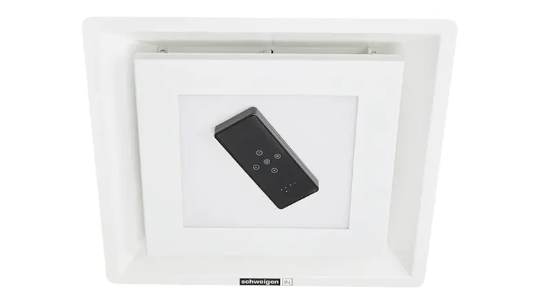 Black remote control sitting on the central light panel of a white ceiling hood Black remote control sitting on the central light panel of a white ceiling hood