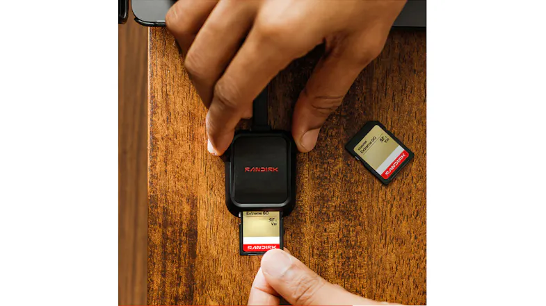 Top-down view of a SanDisk Extreme GO SD card being inserted into a black card reader on a wooden desk Top-down view of a SanDisk Extreme GO SD card being inserted into a black card reader on a wooden desk