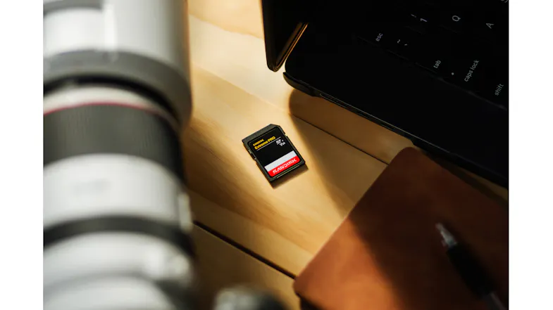 Angled close-up of a black and red SanDisk Extreme PRO SD Card on a wooden desk near a laptop and notebook Angled close-up of a black and red SanDisk Extreme PRO SD Card on a wooden desk near a laptop and notebook