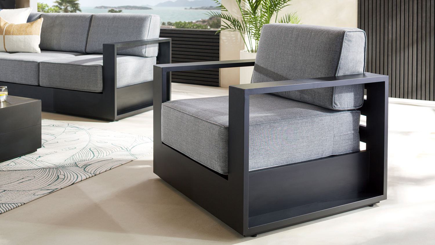 A white‑framed Monaco outdoor chair with grey cushions and a patterned green throw pillow.