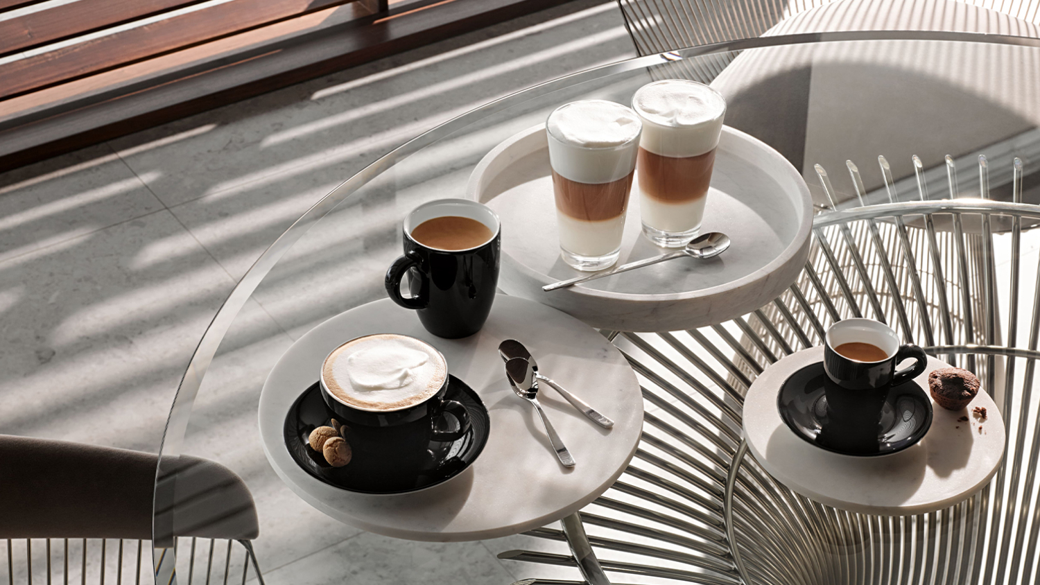 A glass table with different coffee types on saucers.