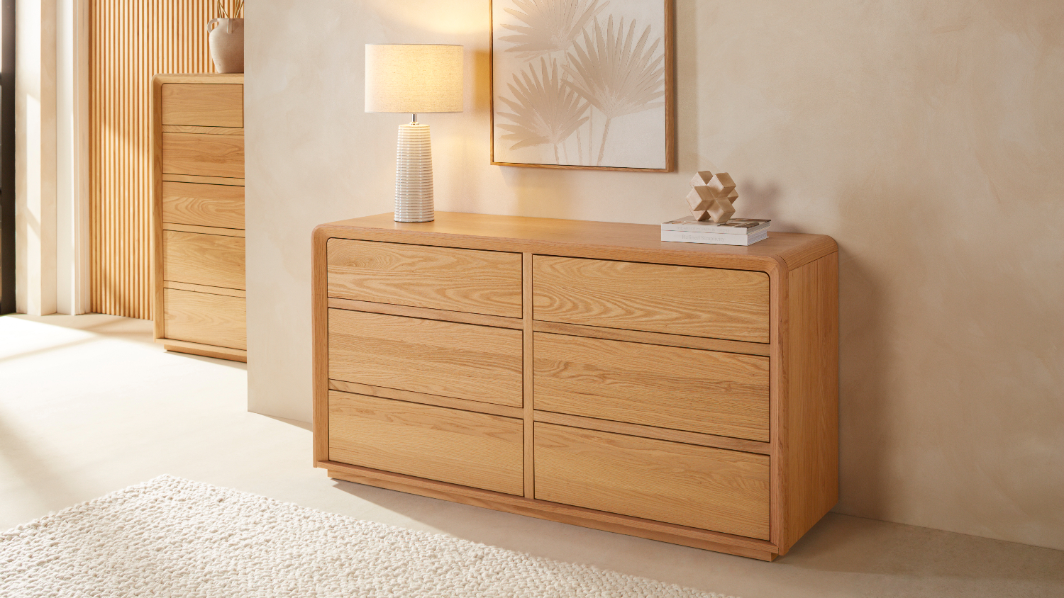 A small wooden lowboy in a bedroom with a lamp and framed art on top.