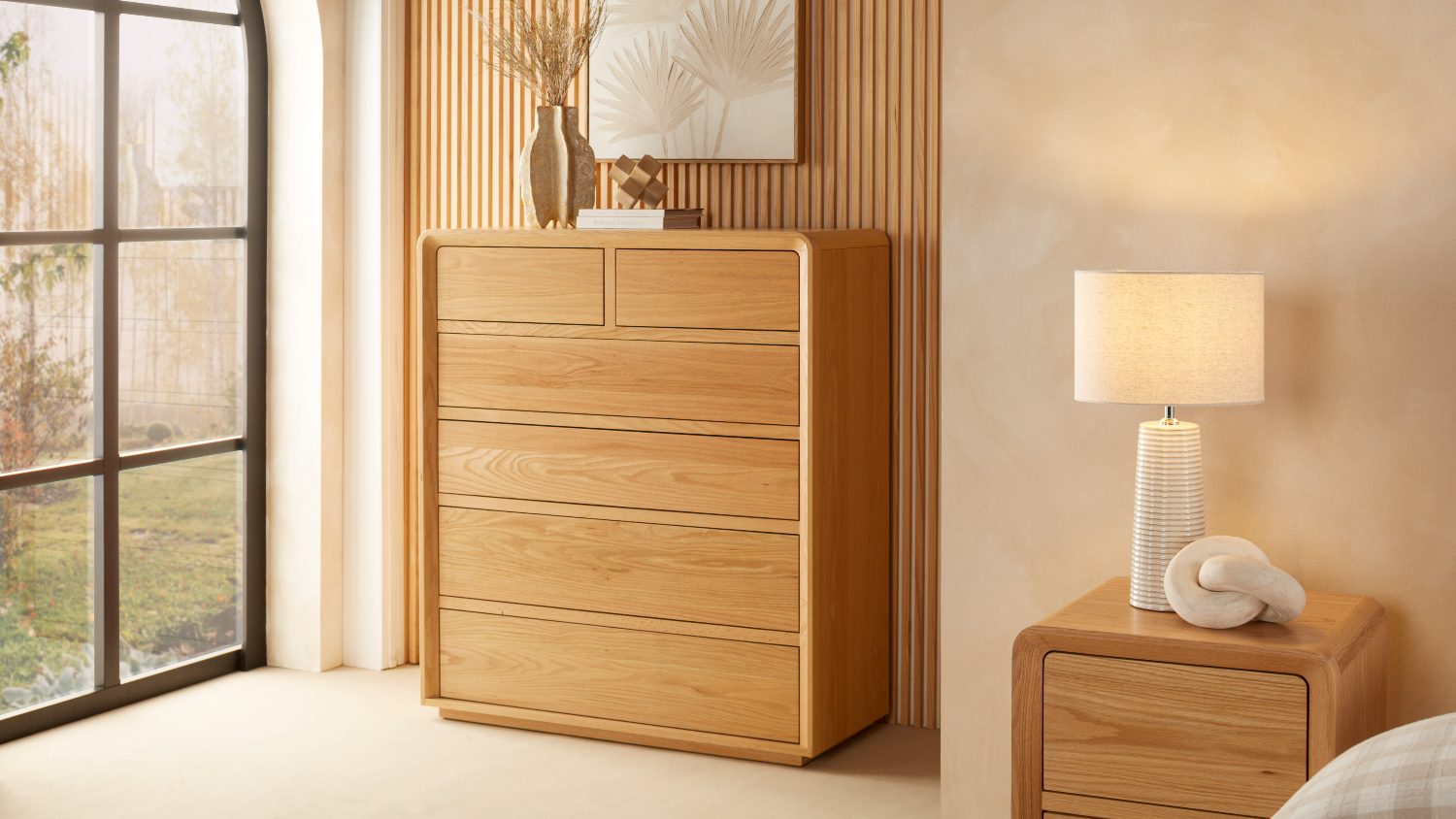 A 6-drawer tallboy in a minimalist bedroom with a large window beside it.