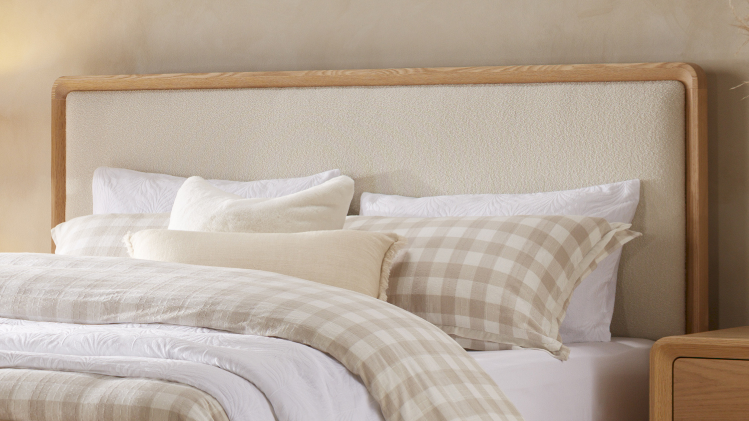 A view of the Omaha Queen Upholstered Headboard, showing its light wooden frame and cream-coloured textured fabric.