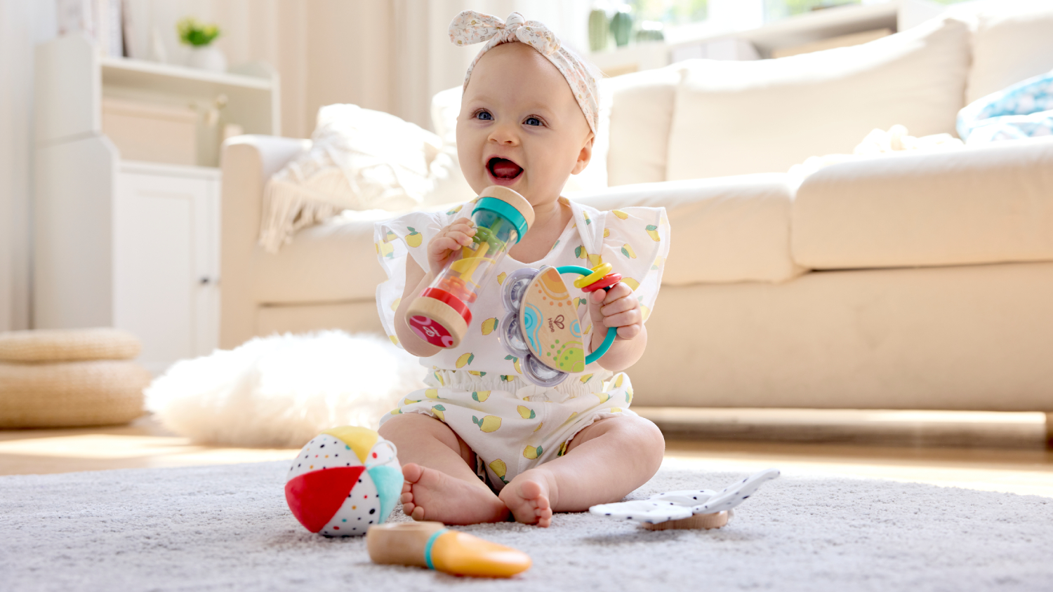 The baby holds colourful toys, including a rattle and a multi-ring toy.