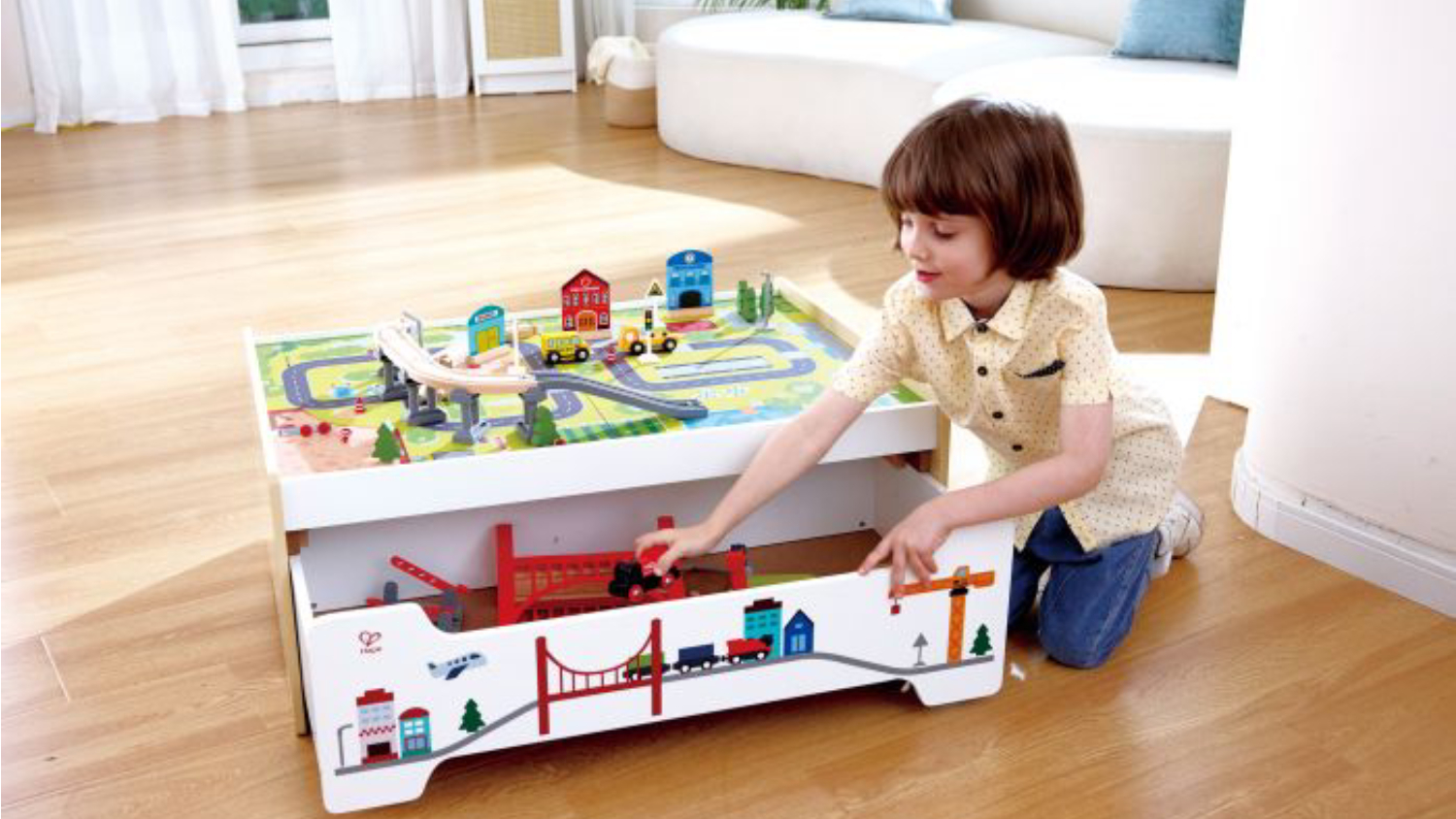 A child kneels on a wooden floor, playing with a wooden train set.