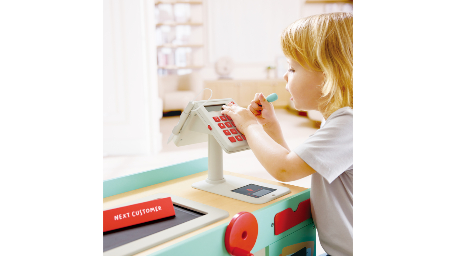 A child playing with a toy cash register featuring a red and white keypad.