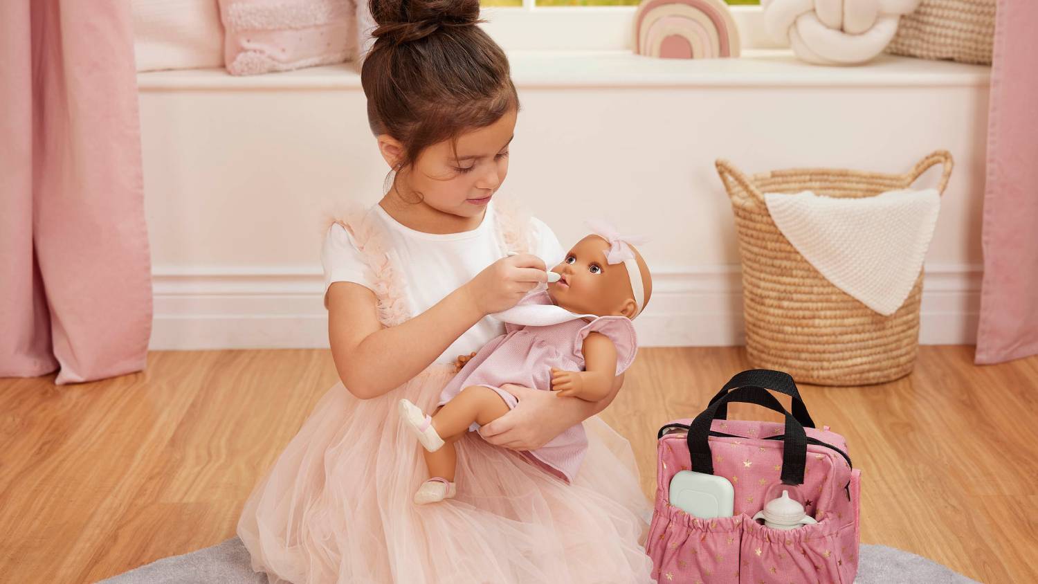 A child sitting on the floor feeding a baby doll with the nappy bag and other accessories nearby