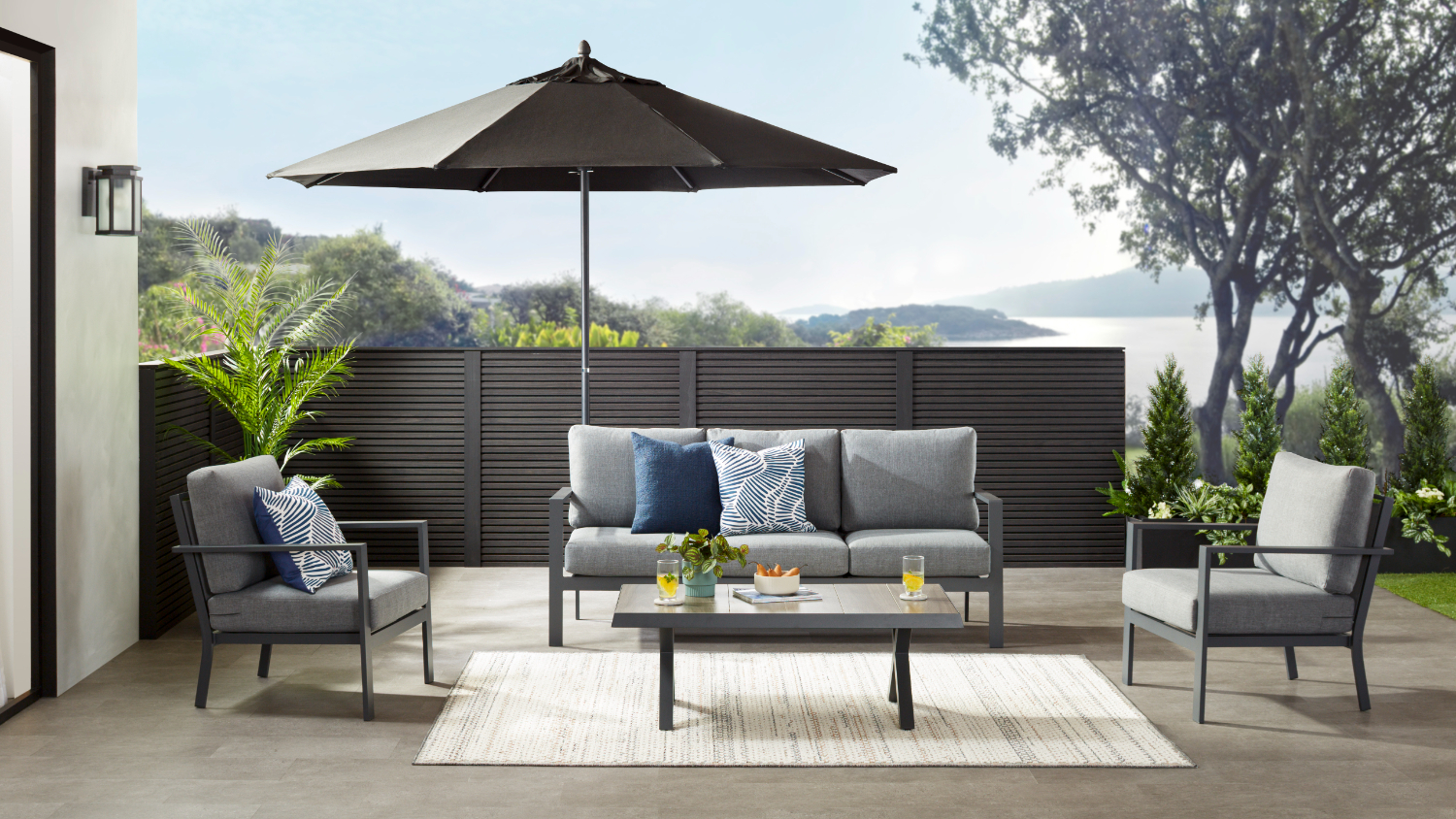 Outdoor lounge suite with a grey sofa, two armchairs, and a coffee table under a black umbrella on a patio