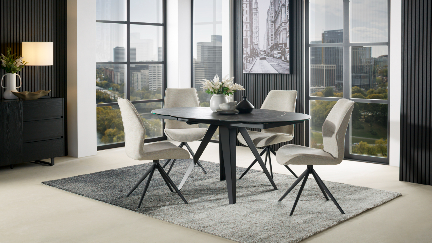 A contemporary dining set with a round black table and four silver chairs on a gray rug.