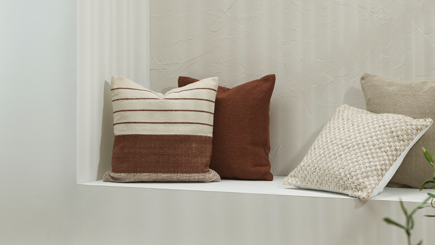 Four cushions on a white bench: striped beige and brown, solid brown, and textured beige.