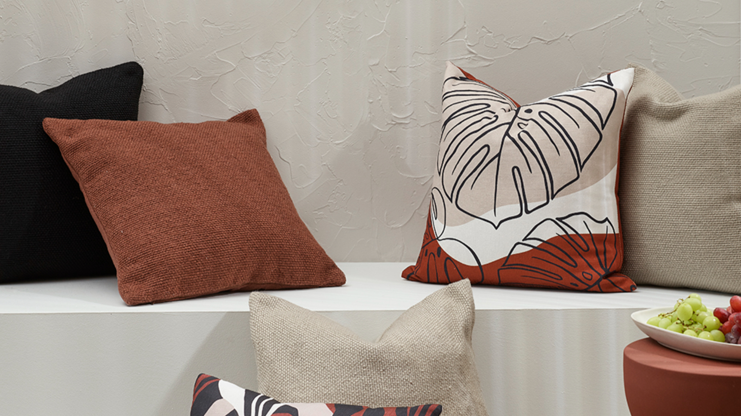 Cushions in various textures, patterns and neutral tones arranged on a bench.