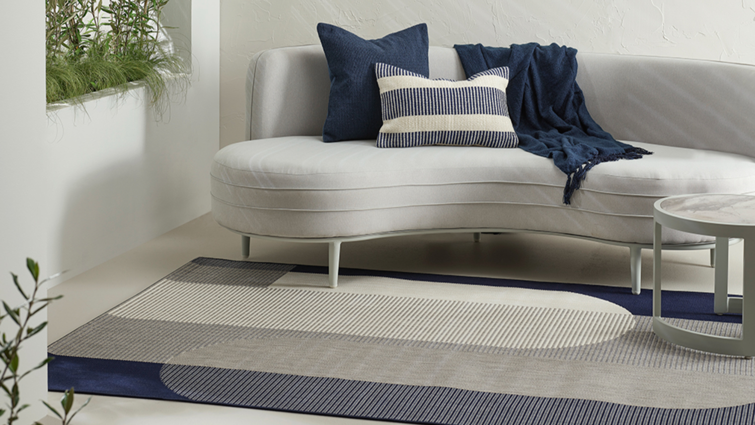 White sofa on a geometric patterned rug with blue and white cushions, and plants nearby.