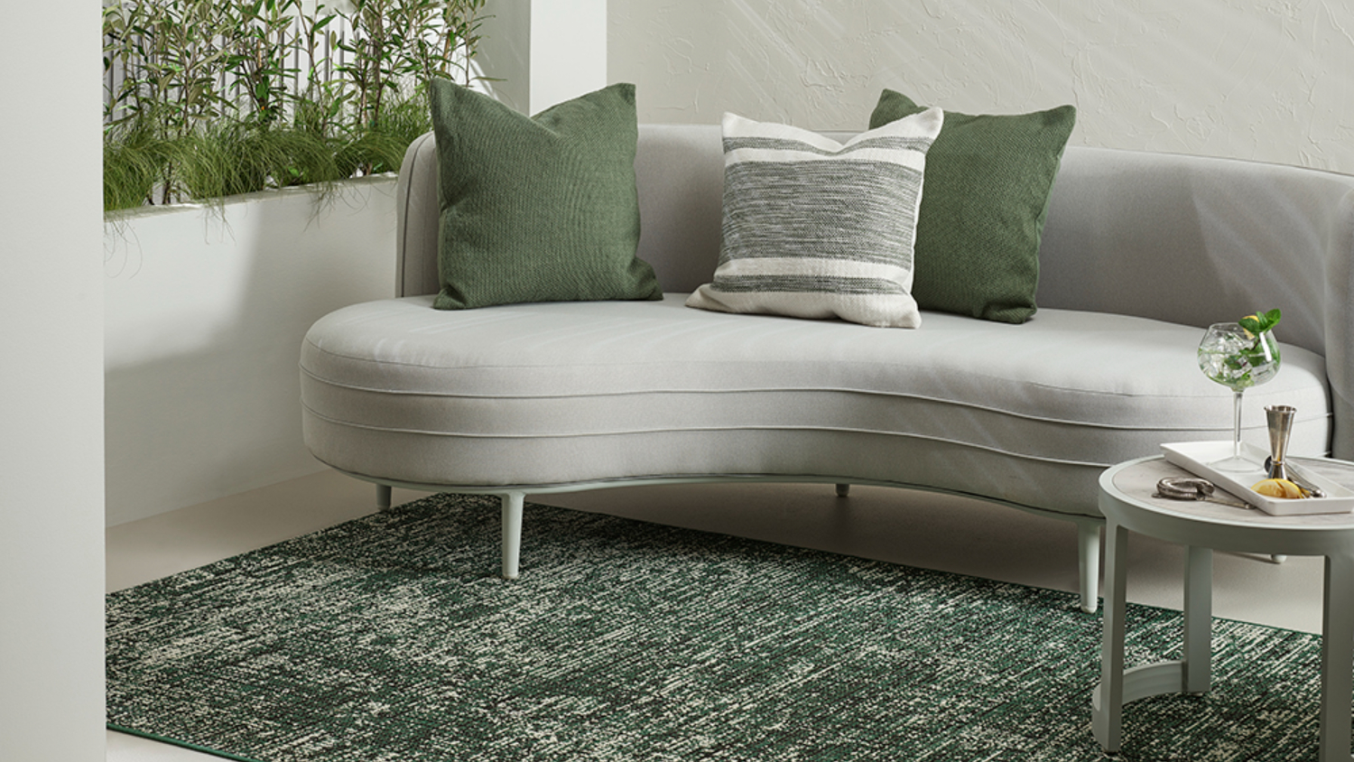 Side view of the green and white textured rug beneath the curved gray sofa with assorted cushions.