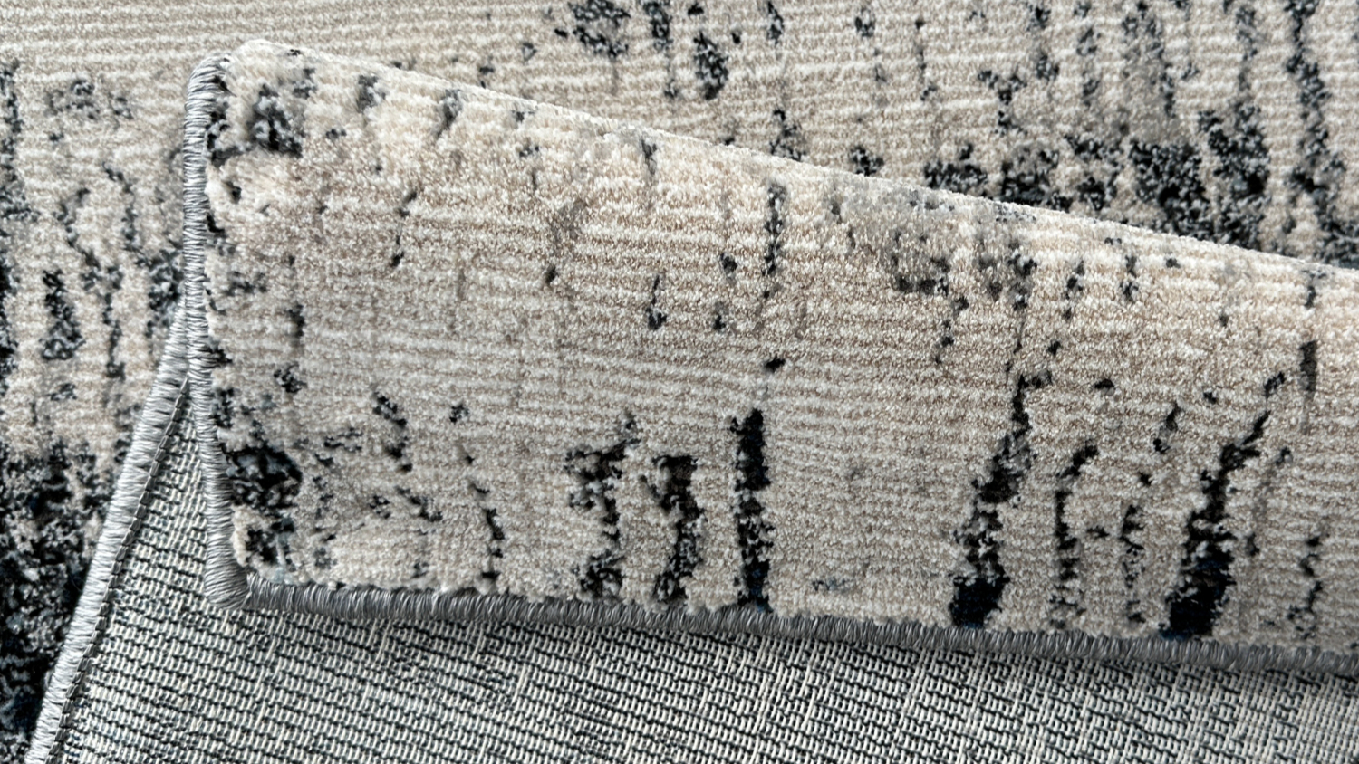 Folded rug corner showing underside of striped black-white-grey rug.