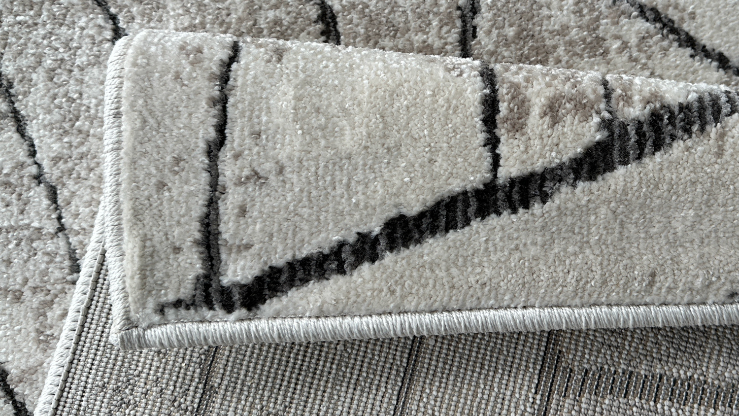 Folded corner of an abstract patterned rug in beige and black tones, showing the texture and backing.