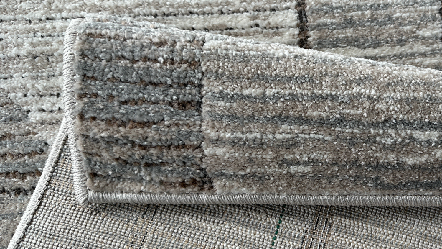 Close-up view of a folded rug corner with a grey abstract design, showing the texture and backing.