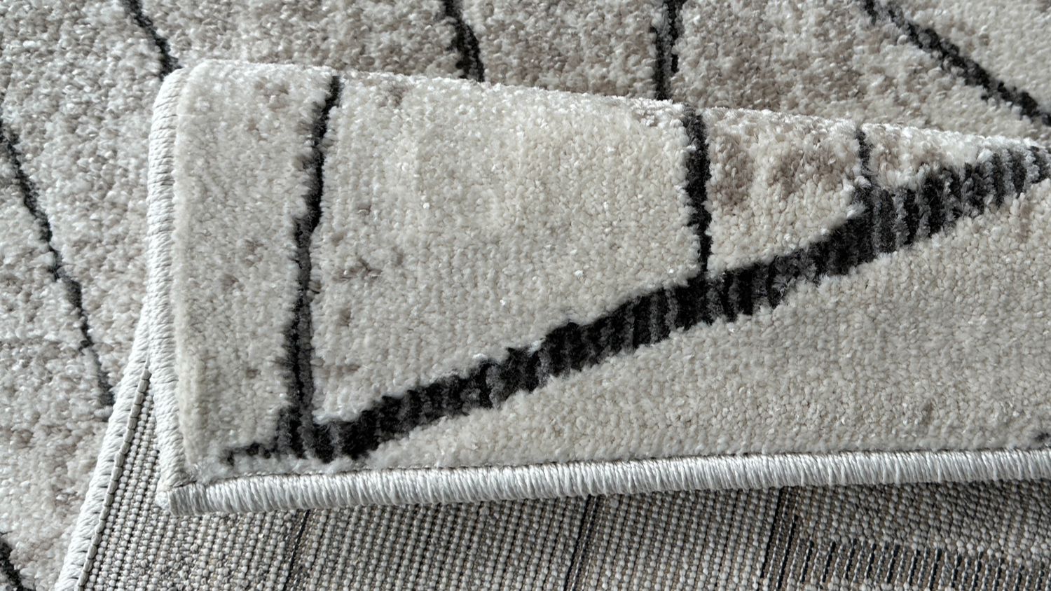 Folded corner of an abstract patterned rug in beige and black tones, showing the texture and backing.