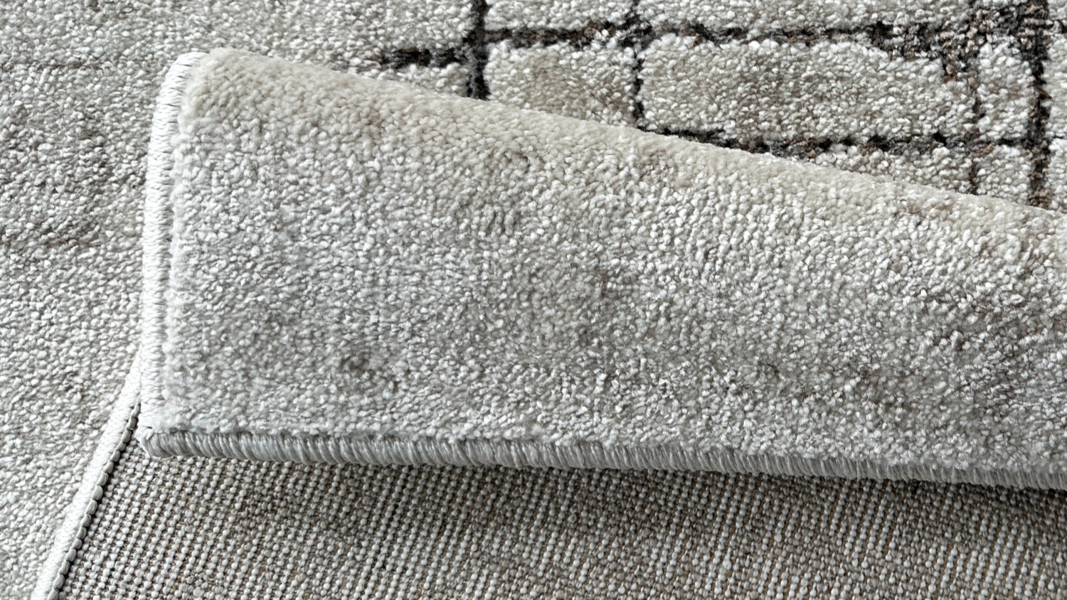 Rug corner folded to reveal underside, showing texture and detailed grid-like design in grey tones.