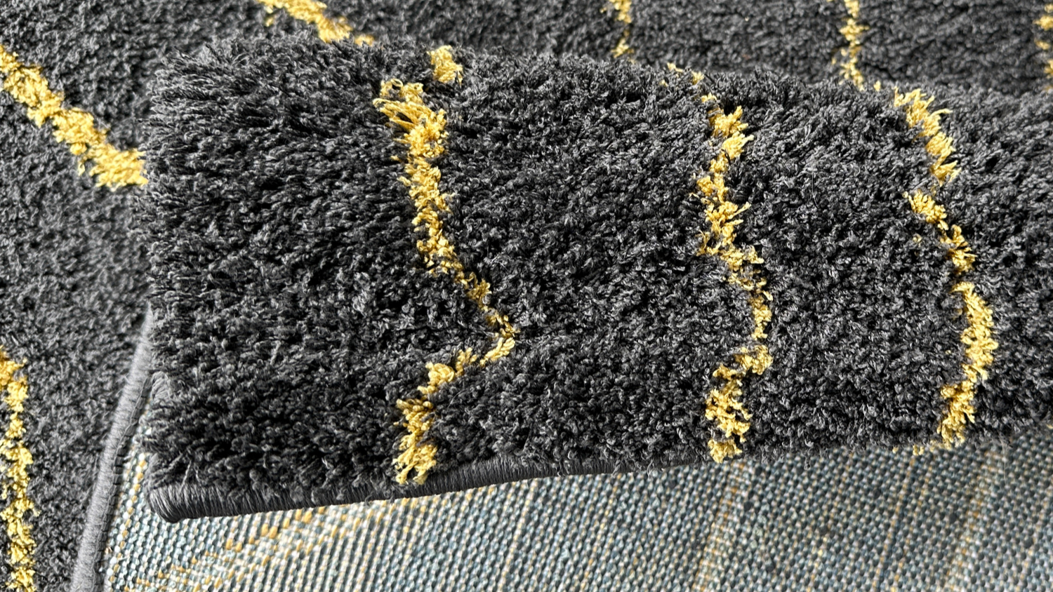 Folded grey rug corner showing yellow line pattern and underside.