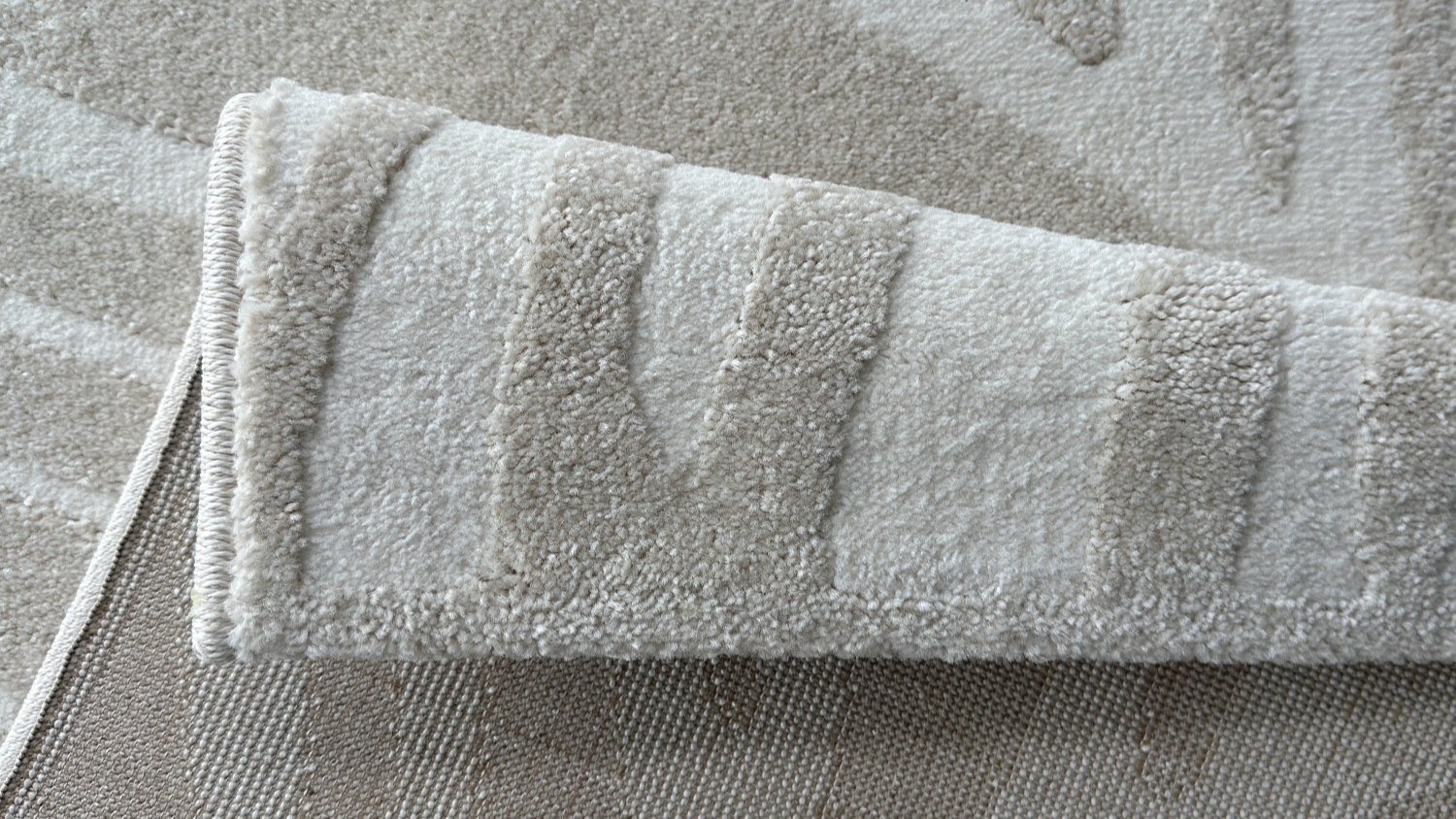 Folded corner of light grey rug showing thickness and texture.