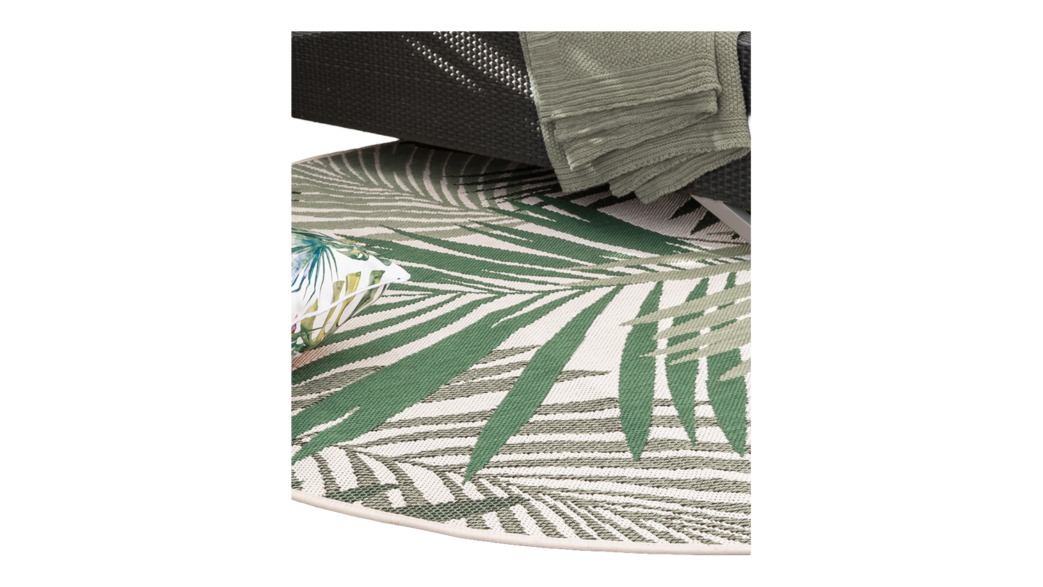 The rug is placed under outdoor furniture, showcasing its tropical palm leaf design in a real-life setting