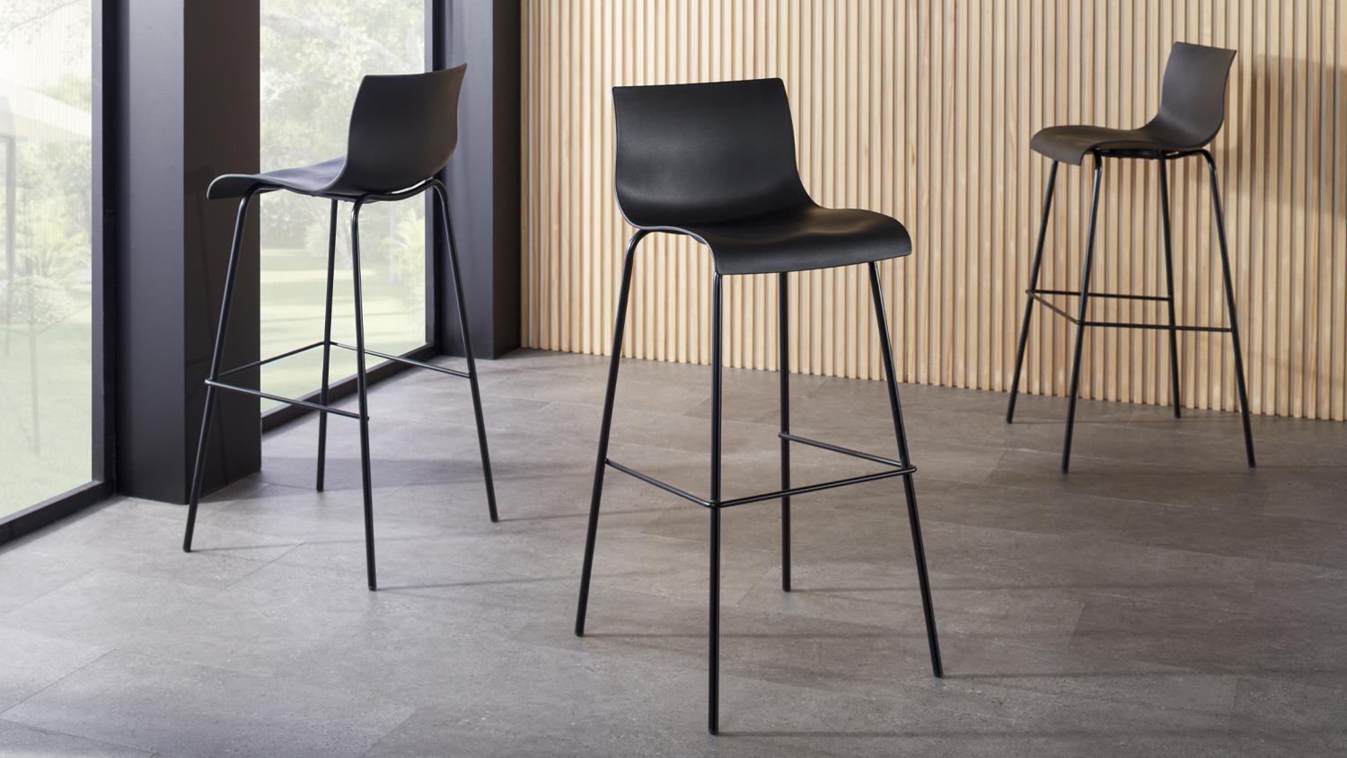 Black Levy Bar Stool with a smooth, curved seat and low backrest, supported by four slim metal legs with a footrest
