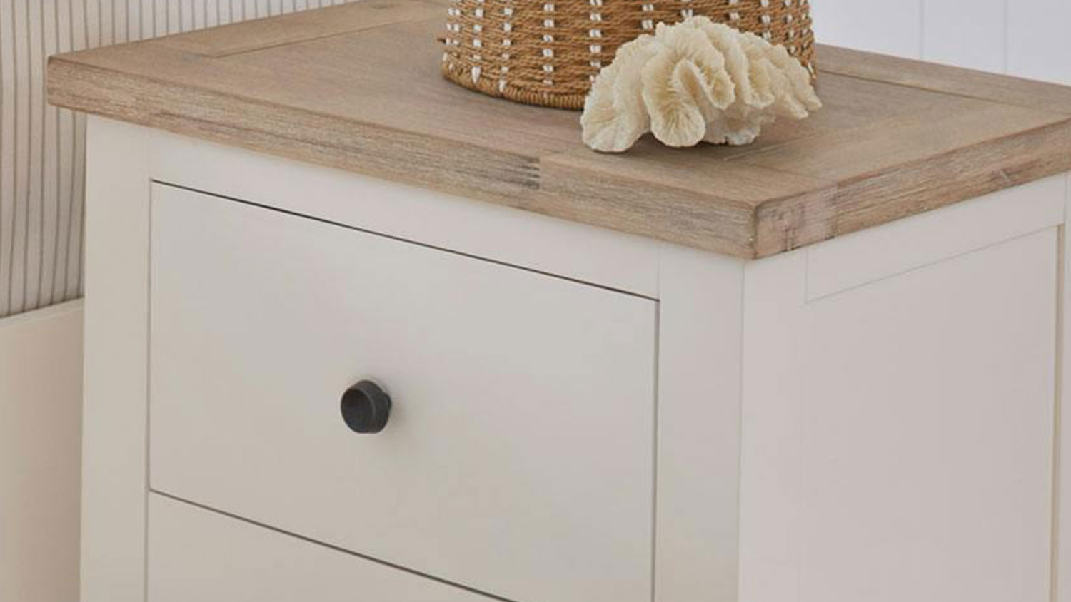 Taylor 2 Drawer Bedside Table shown with a decorative shell and basket sitting on it, beside a bed.