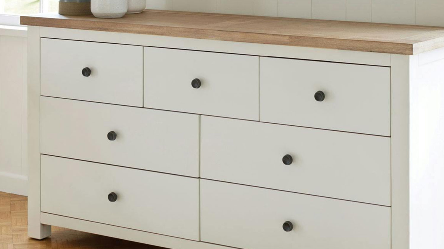 Taylor 7 Drawer Lowboy with décor sitting on top, against a bedroom wall between two windows.