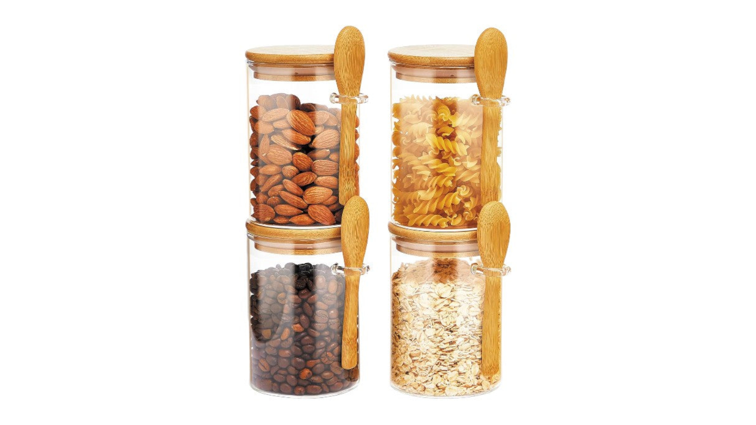 Four glass jars with bamboo lids and attached spoons filled with almonds, pasta, coffee beans, and oats