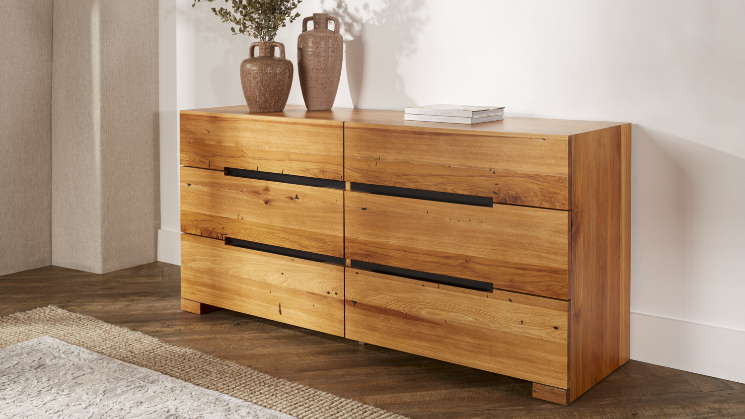 Full view of a six-drawer wide dresser made of natural wood with dark recessed handles in a contemporary room
