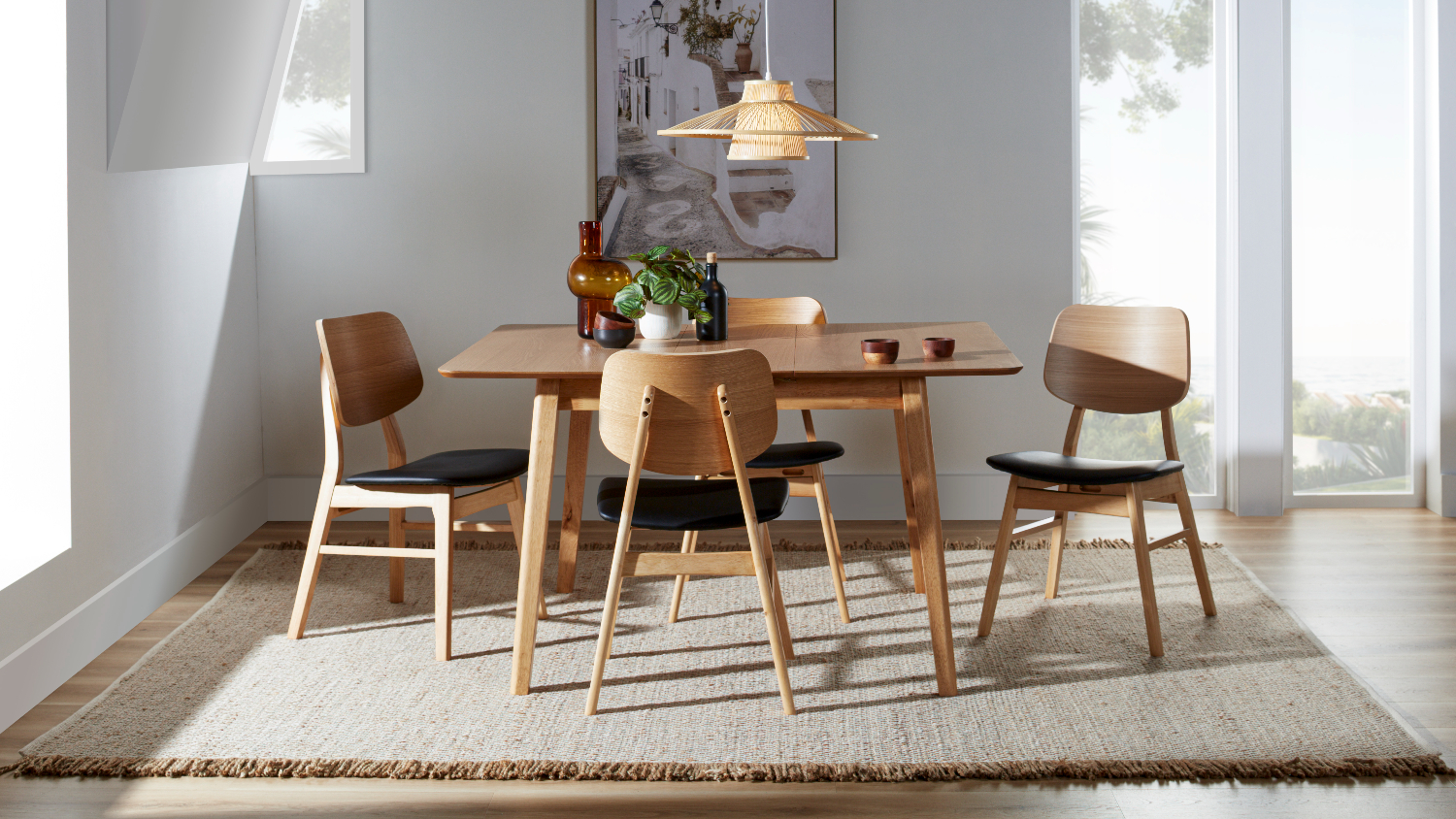 Close-up of a light wood dining table surface with two small wooden bowls and a green potted plant