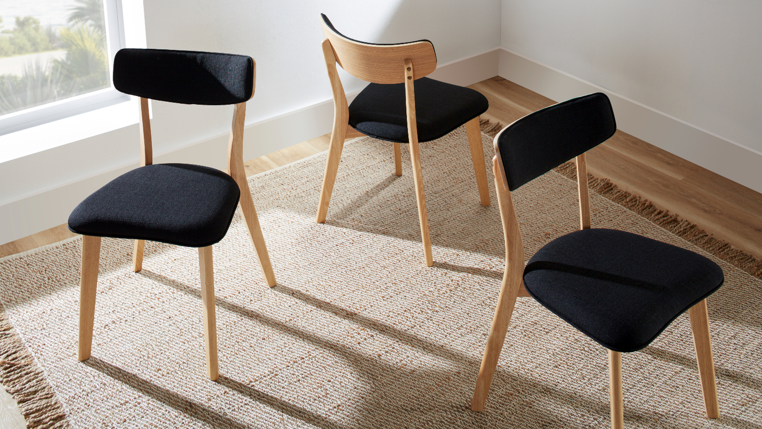 Three Zara dining chairs with black fabric seats and backs, light wooden frames, arranged on a beige textured rug
