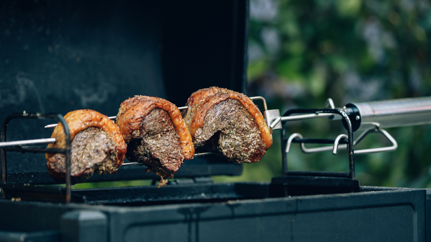 A view of large cuts of meat being rotated and roasted over a BBQ