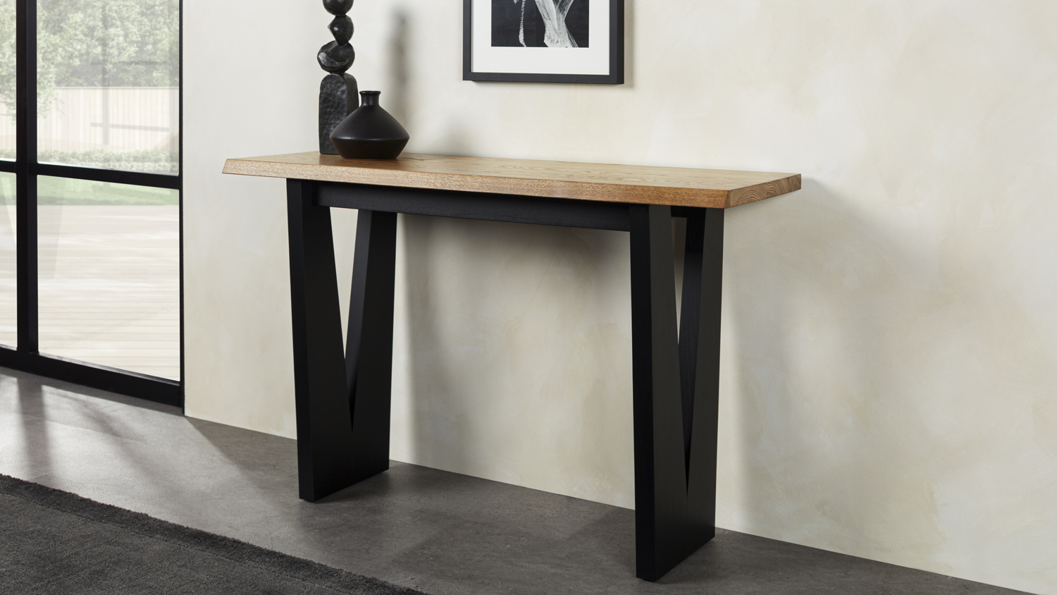 Raglan Hall table with a natural wood top and black angular legs, with decorative items placed on the surface