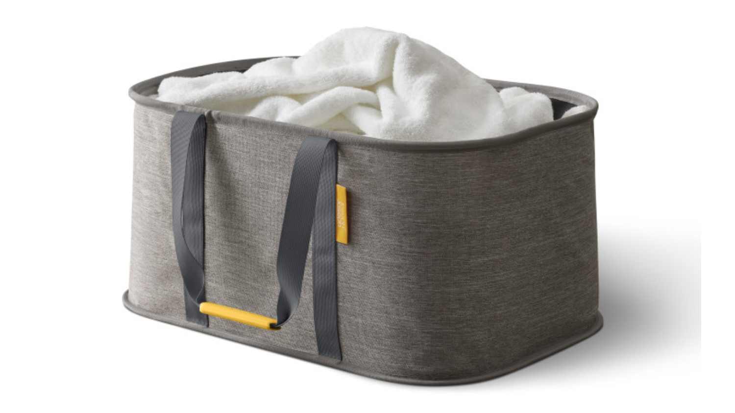 A grey fabric storage basket with dark handles holding a white fluffy blanket