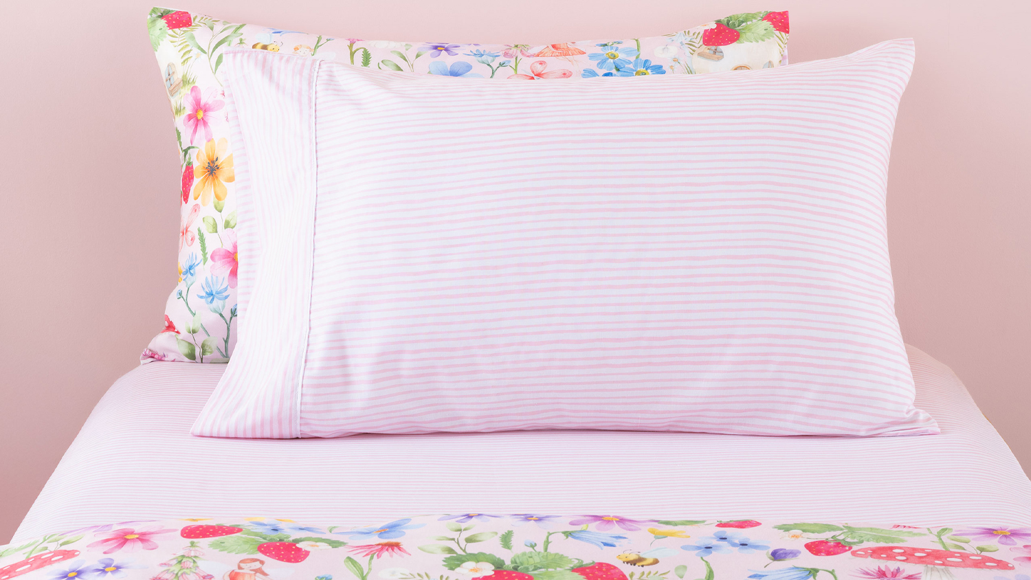 A cosy bed setup featuring Squiggles pink striped sheets paired with colorful wildflower patterns.