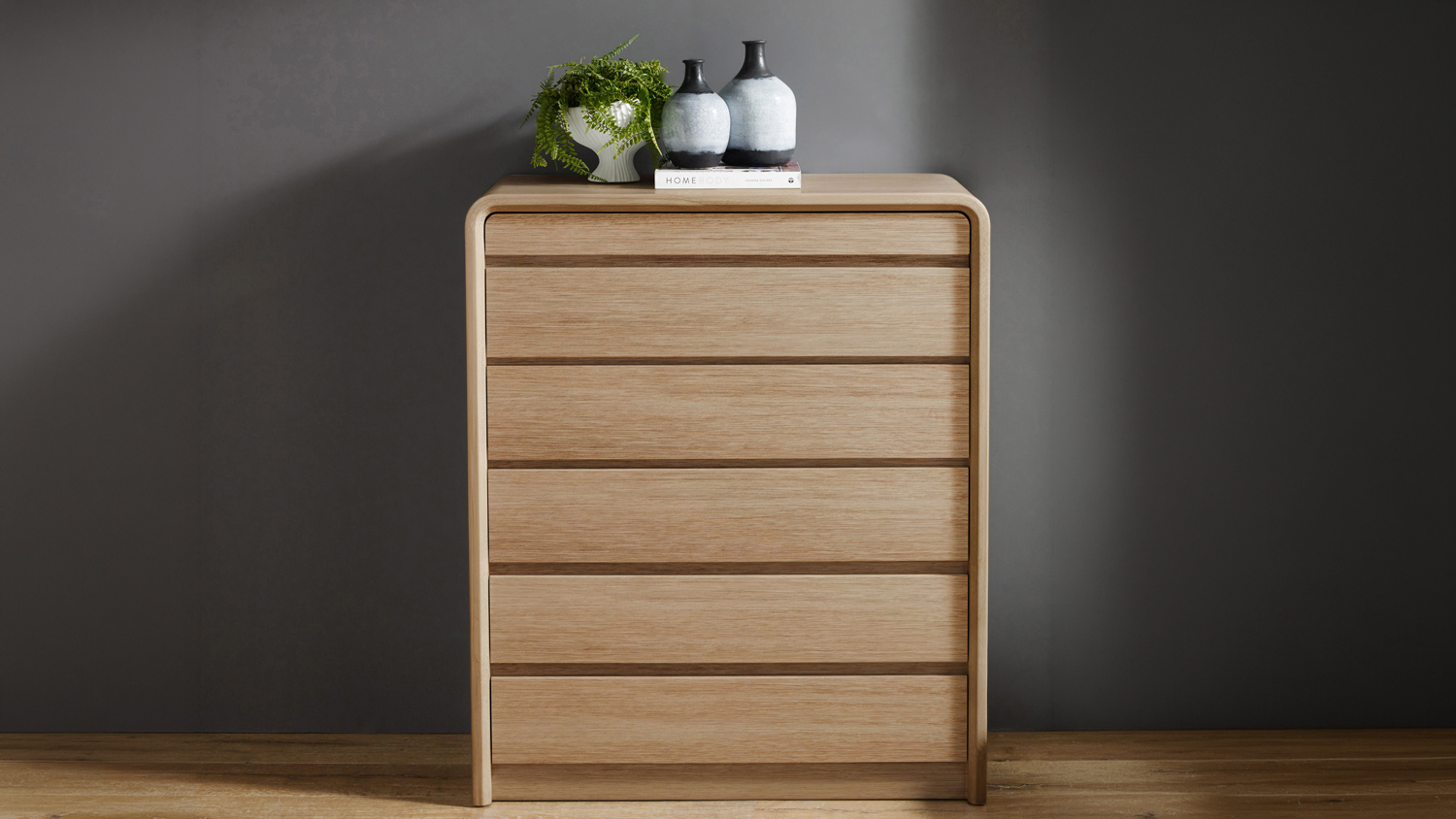 Front view of the Arc 6 Drawer Tallboy in light wood against a dark grey wall