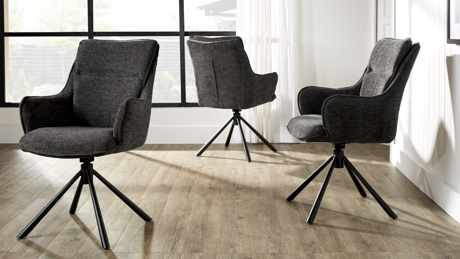 A set of three charcoal upholstered bar stools arranged in a bright room with wood flooring