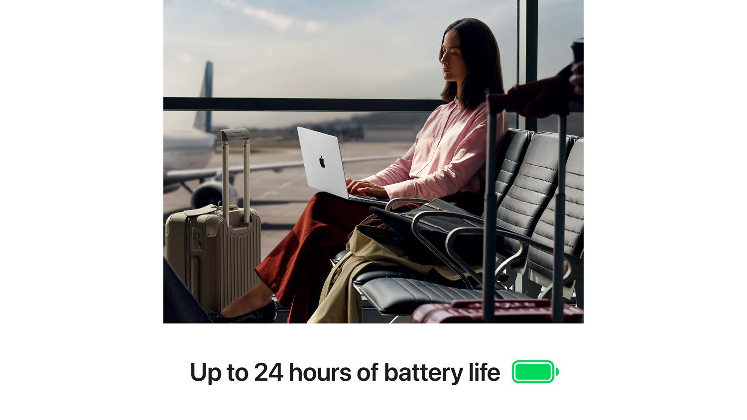 A person seated in an airport lounge working on a MacBook Pro with luggage beside them